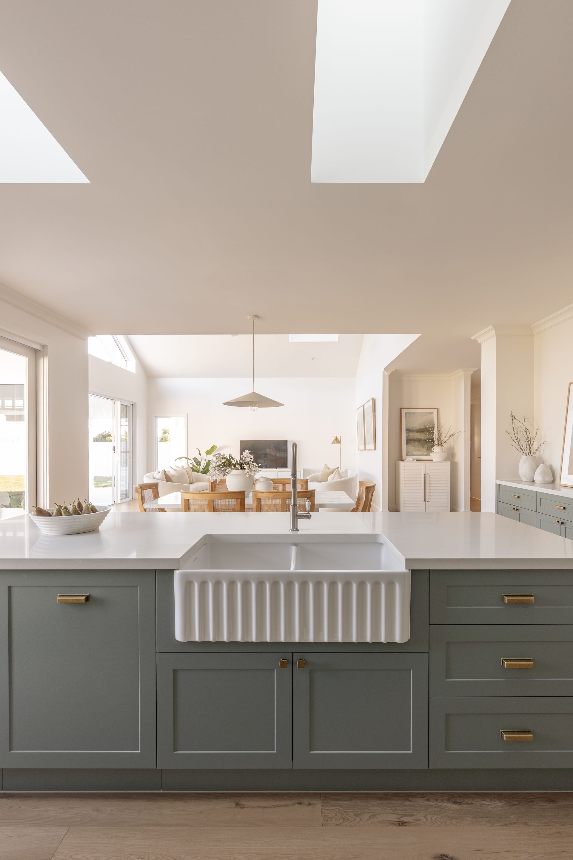 Green kitchen island with farmhouse sink, looking into a bright dining area.