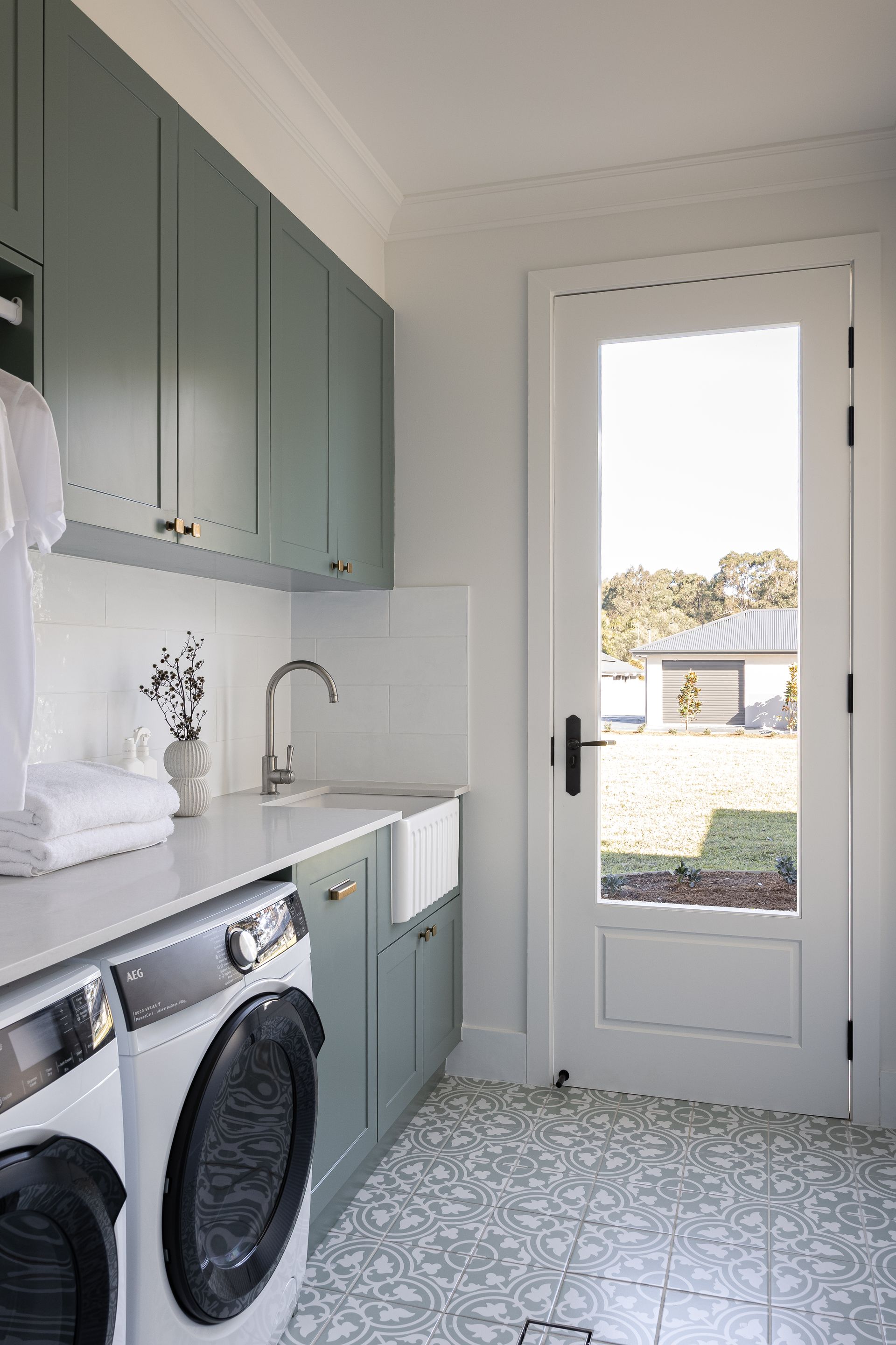 Laundry room with green cabinets, white countertop, and patterned floor; a door reveals the outdoors.