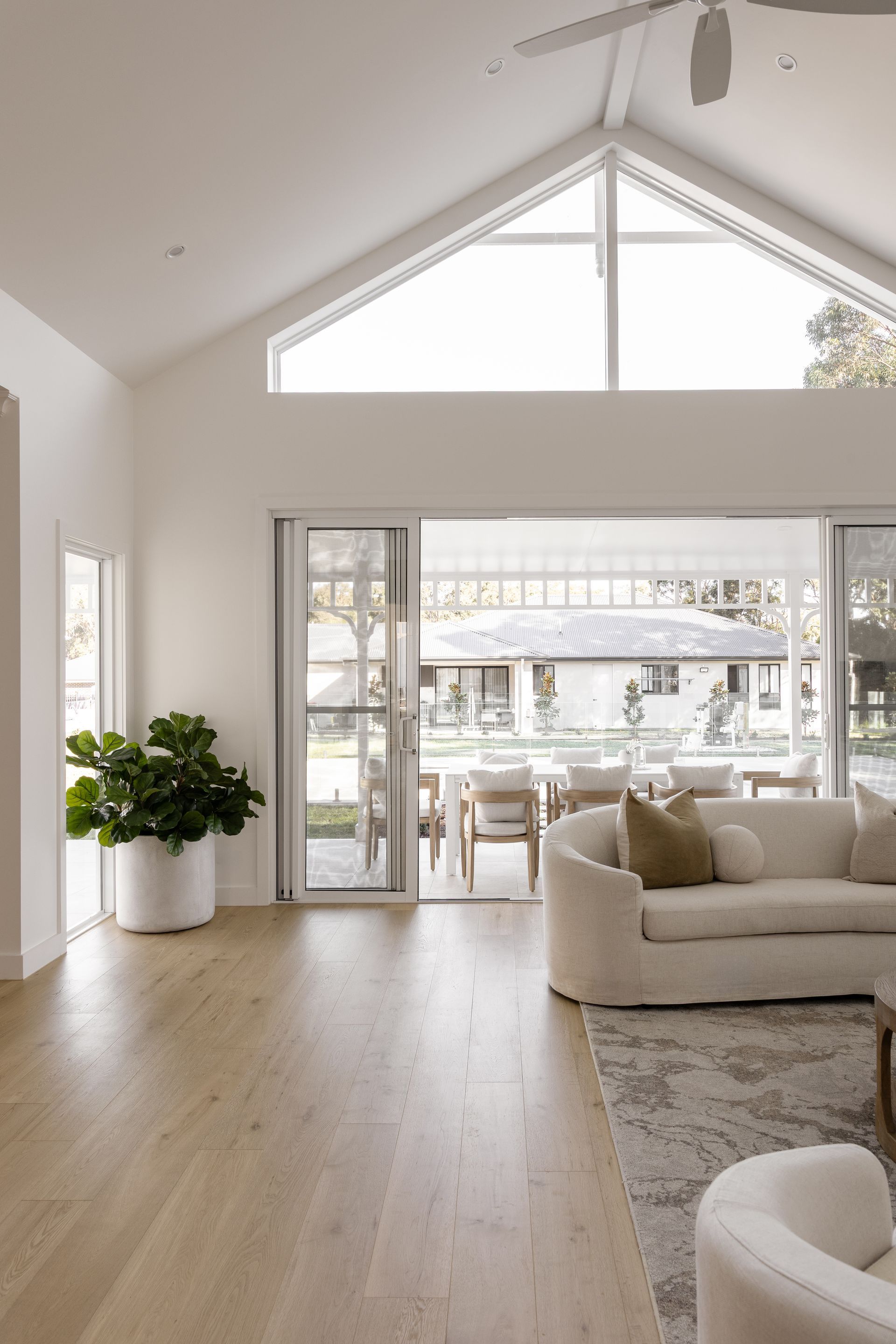 Bright living room with a high ceiling, large windows, and a view to an outdoor dining area.