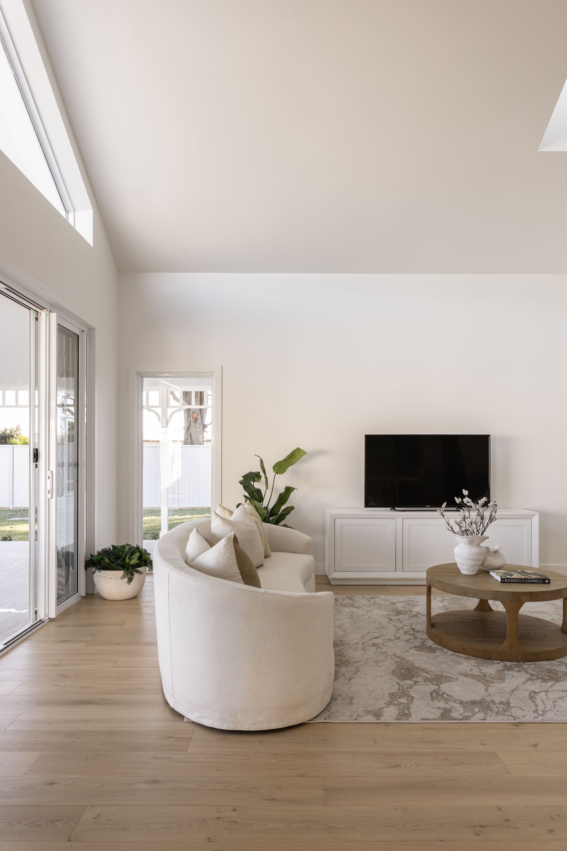 Living room with curved white sofa, TV, and wooden coffee table.