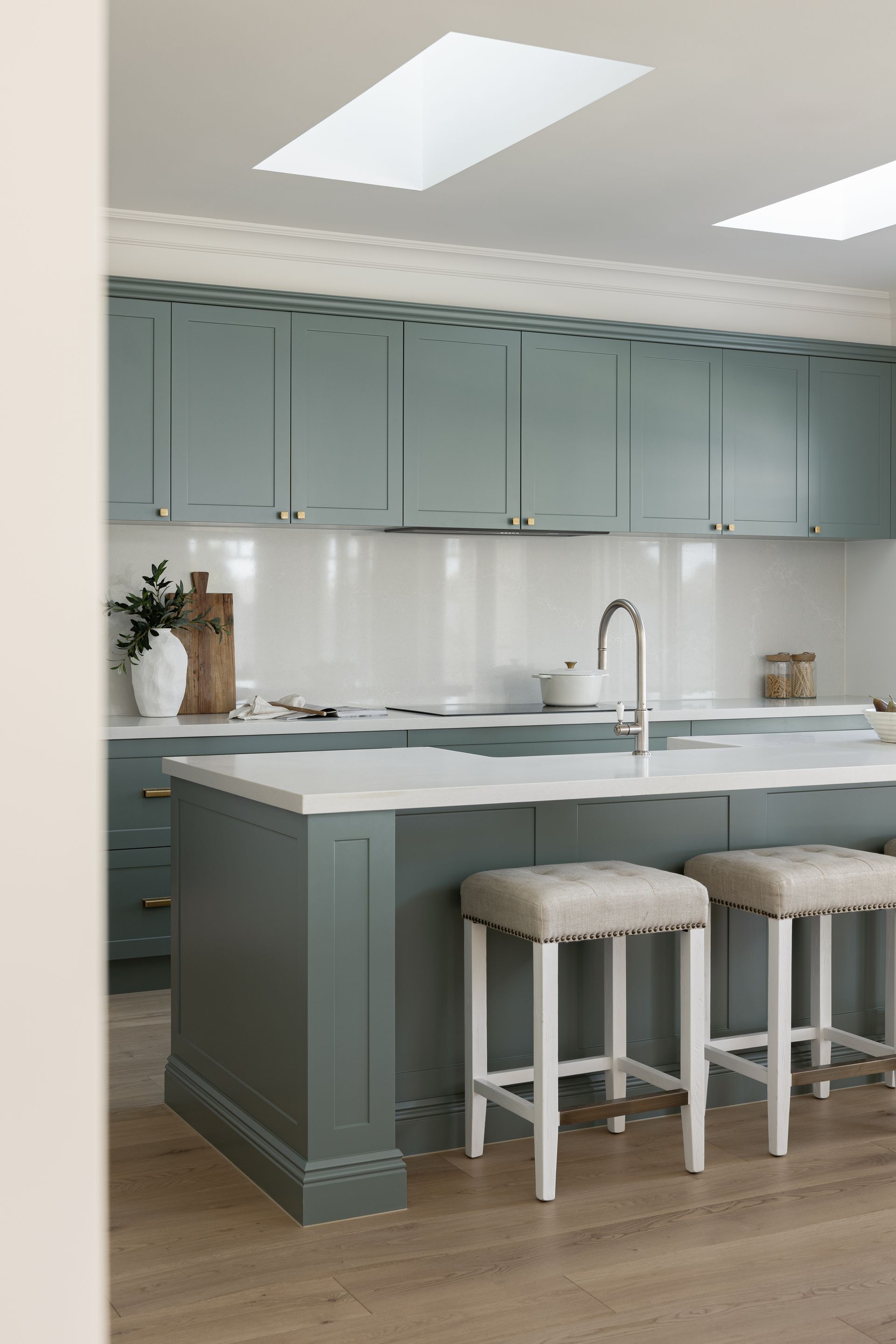 Kitchen with teal cabinets, white countertops, island with stools, skylights, and light wood floor.
