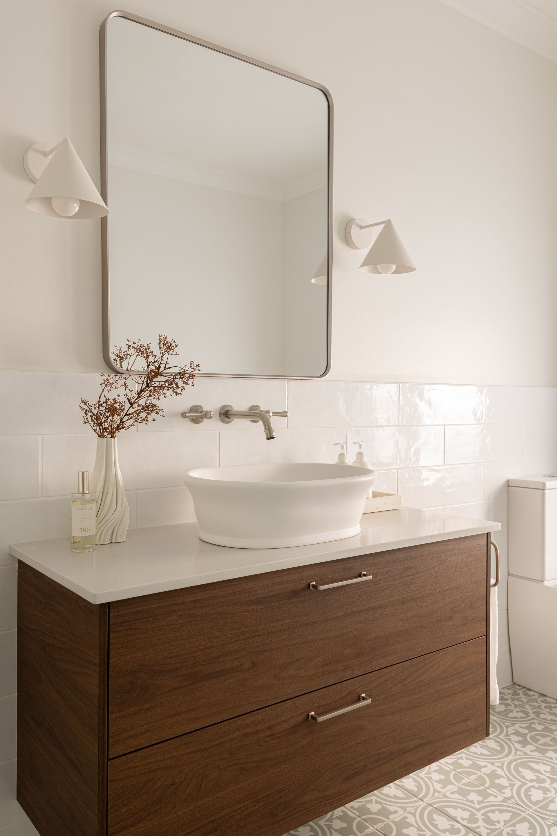Bathroom with wooden vanity, white vessel sink, large mirror, and sconces; white and brown tones.