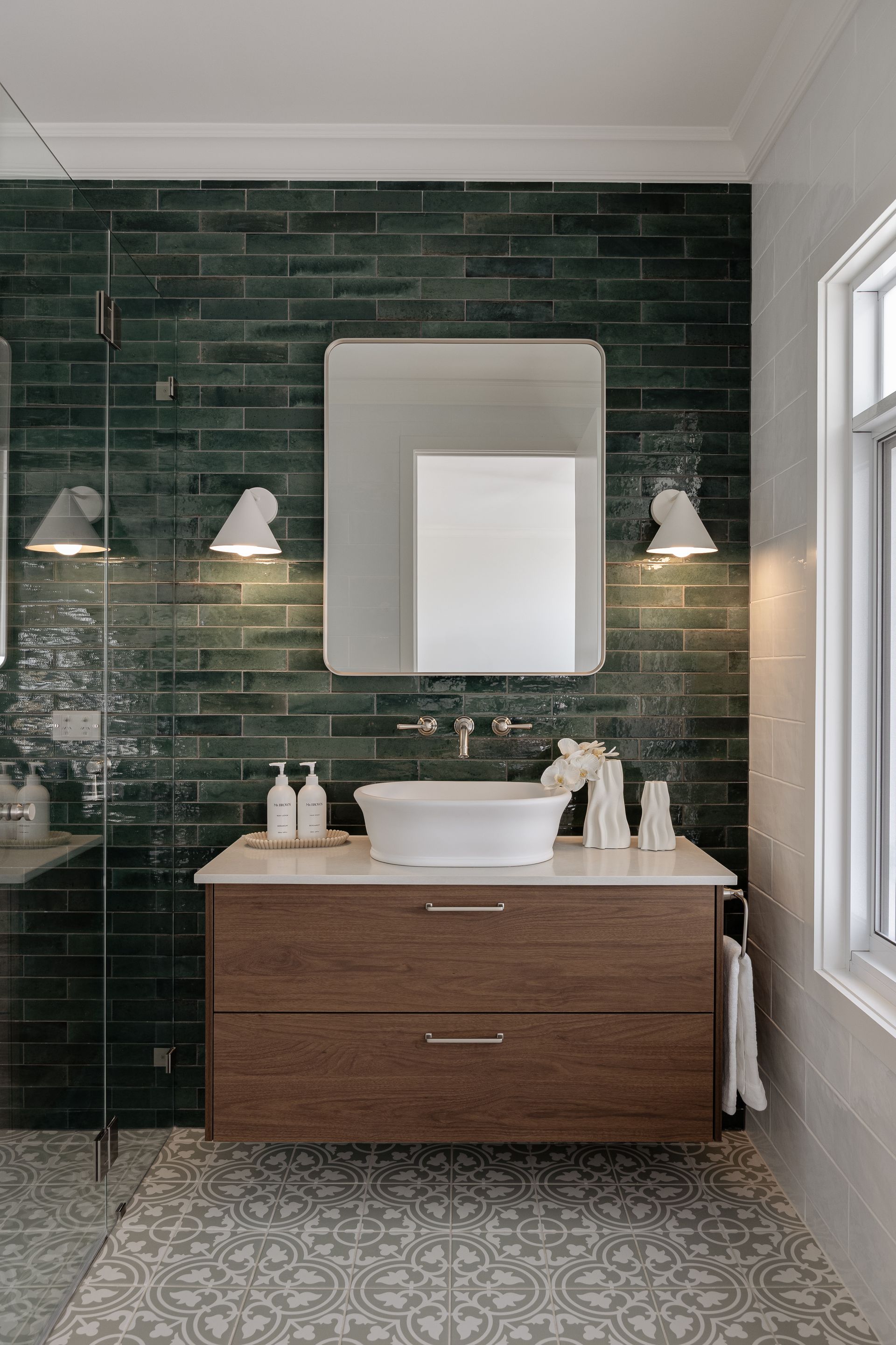 Bathroom with floating wooden vanity, green tiled wall, round sink, and mirror.