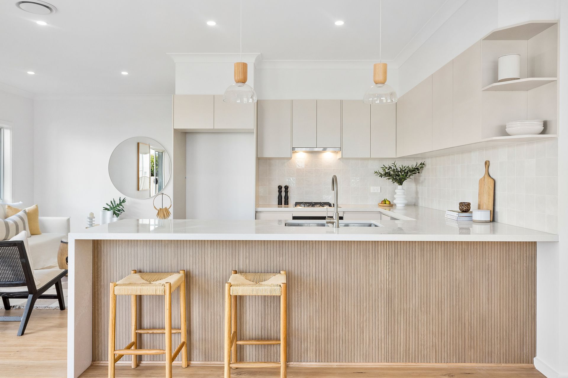 Modern kitchen with light wood accents, white countertops, and bar stools.