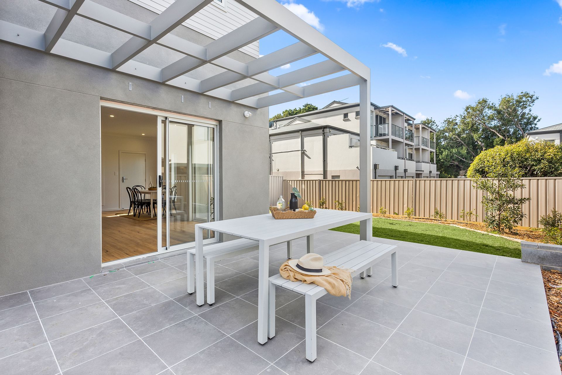 Patio with a table and benches under a pergola. Sliding glass door leads inside.