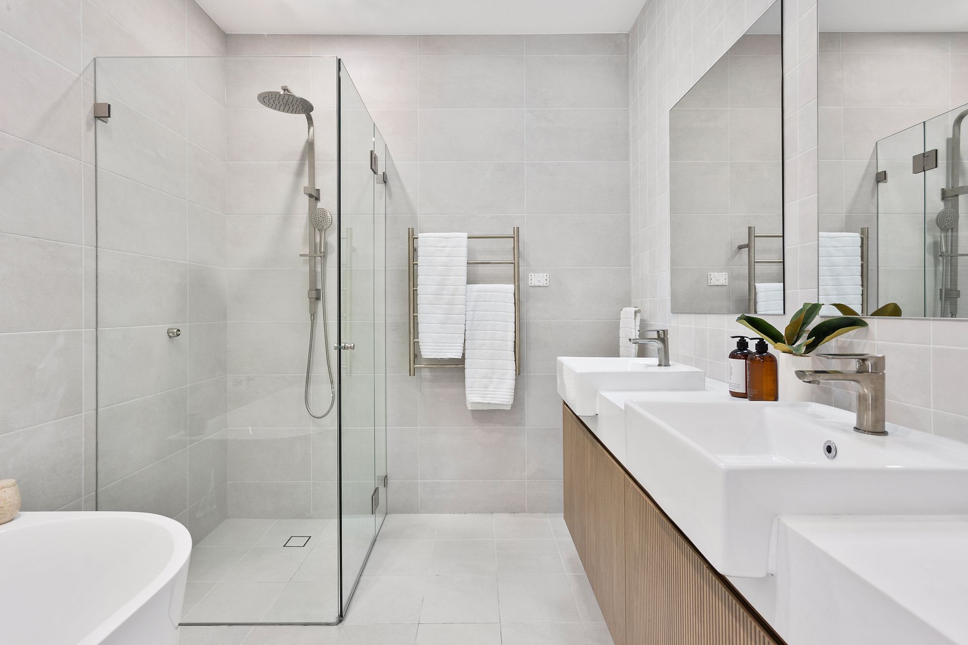 Modern bathroom with a glass shower, double sinks, and light-colored tiles.