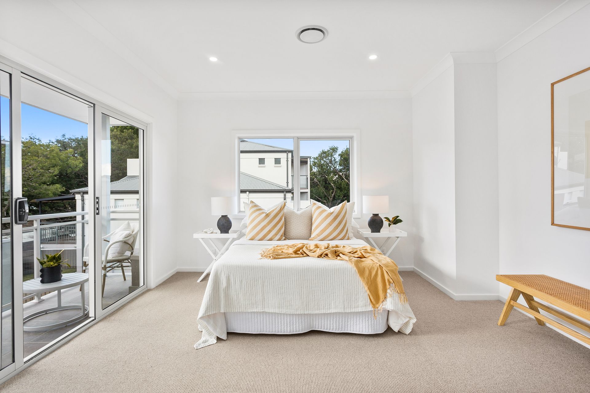 Bedroom with a bed, balcony, and window. White walls, patterned carpet, and yellow accents.