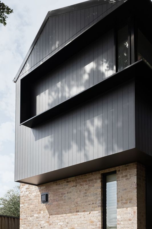 Black modern house with brick base, recessed balcony, and vertical wood siding.