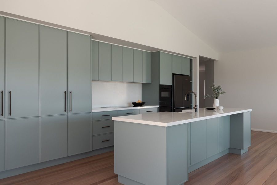 Modern kitchen with sage-green cabinets, white countertops, and a large island; wood flooring.