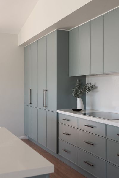 Blue-green kitchen cabinets with black handles; countertop with vase and stovetop; light wood floor.