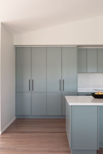 Light blue kitchen cabinets with a white countertop and wooden floor.