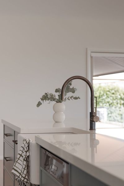 Kitchen island with faucet and vase of eucalyptus. Dishwasher, drawers, and towel visible.