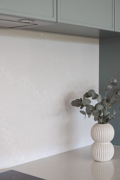 Kitchen backsplash with white textured tiles, green cabinets, and vase with eucalyptus.