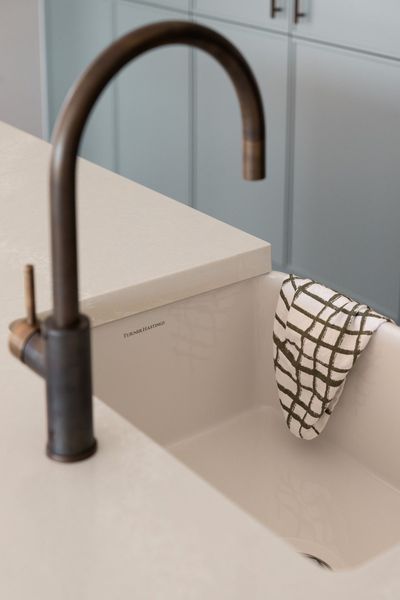 Bronze faucet over a light-colored sink with a checkered towel hanging on the side.