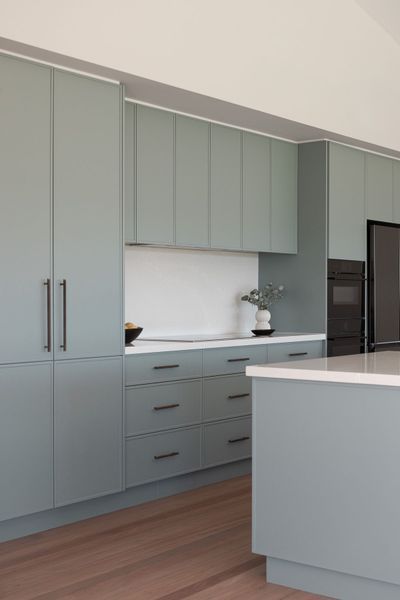 Sage green kitchen cabinets with black hardware, white countertop, and wooden floor.