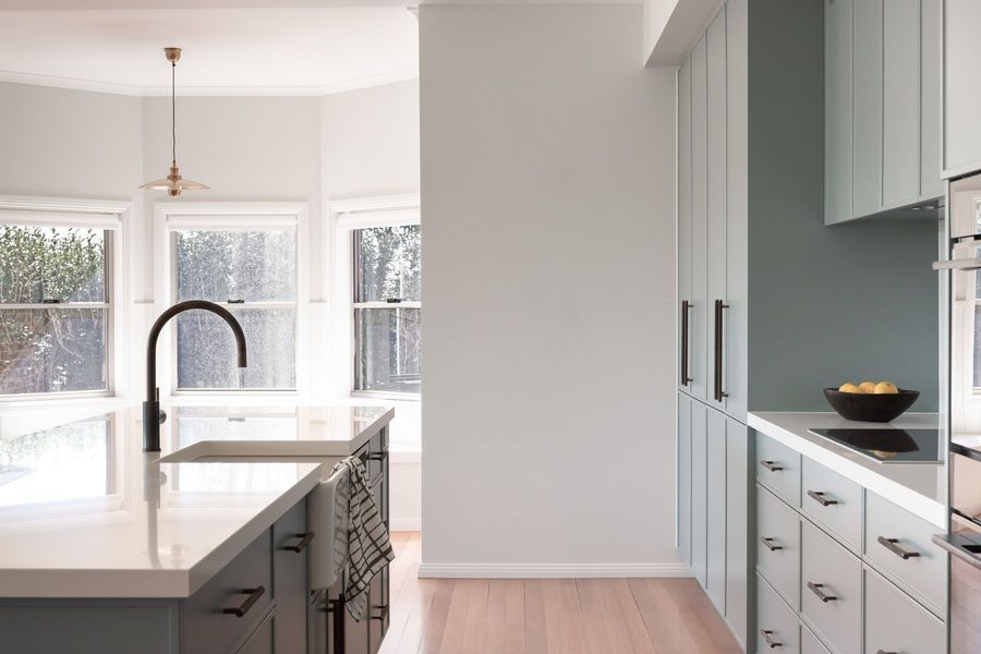 Modern kitchen with light blue cabinets, white countertops, and large windows.