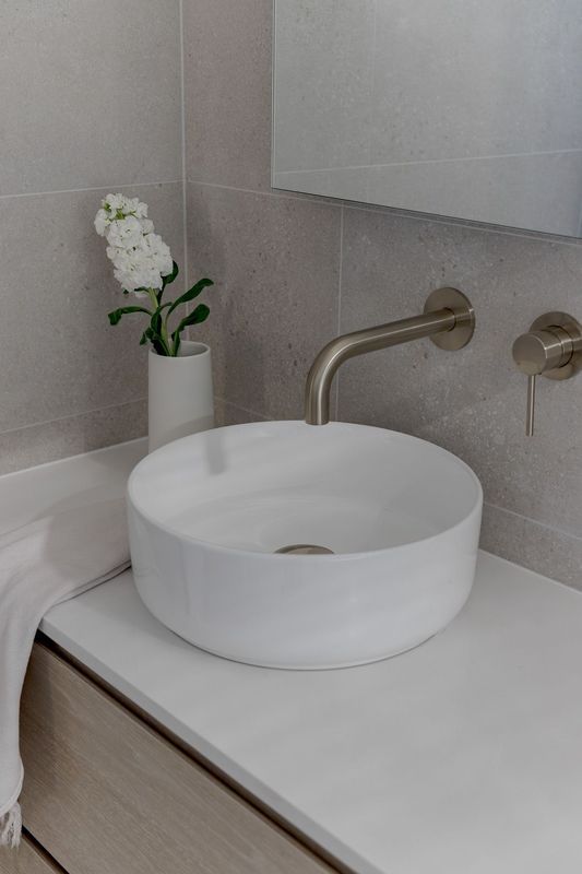 White vessel sink on a white countertop, with a wall-mounted faucet.
