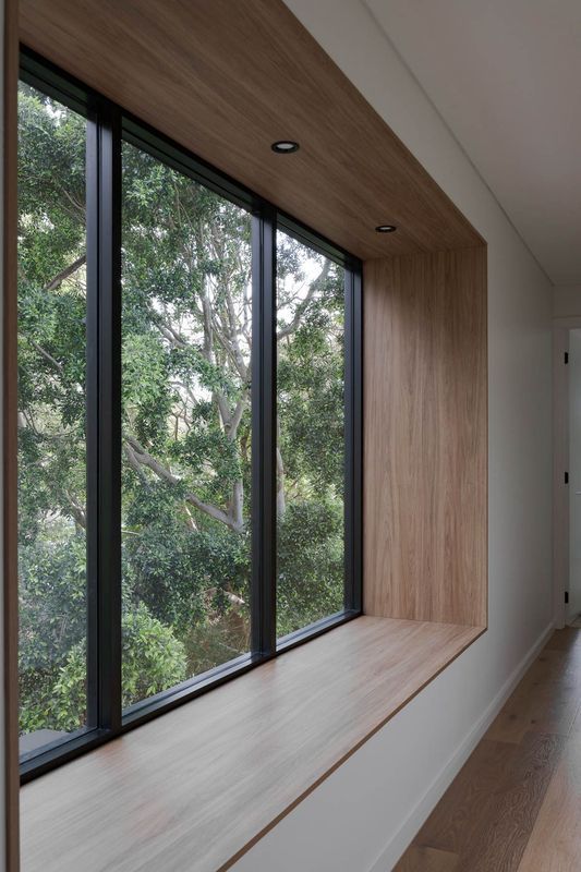 A large window with a wooden frame and ledge, overlooking lush green trees.