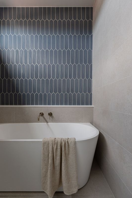 Bathroom with blue elongated tiles, white tub, and beige towel.