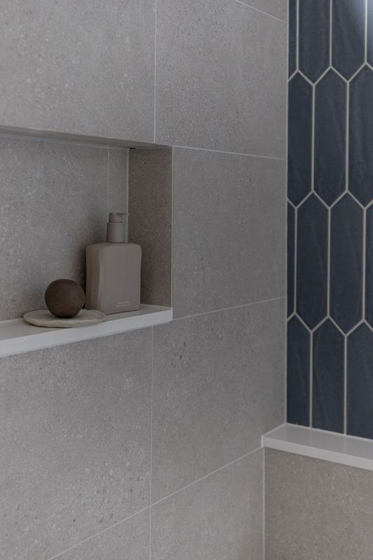 Shower with light gray tiles, built-in shelf with toiletries, and blue, geometric-tiled accent wall.