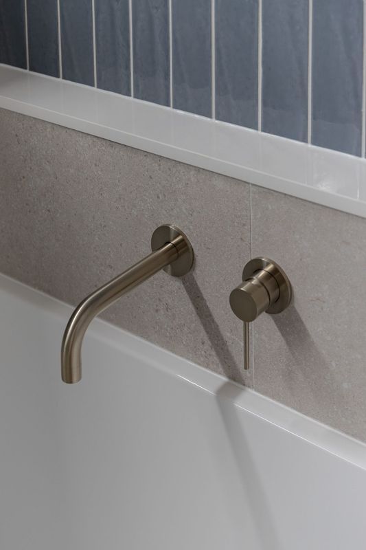 Brushed nickel wall-mounted faucet and control near a white bathtub, against a gray tiled wall.