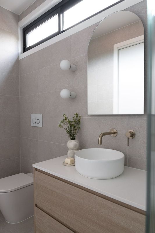 A modern bathroom with a floating vanity, round sink, arched mirror, and wall-mounted gold faucet.
