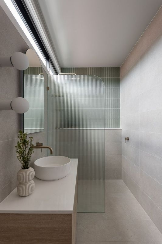 Bathroom with a white countertop, sink, and glass shower door, featuring green textured wall tiles.