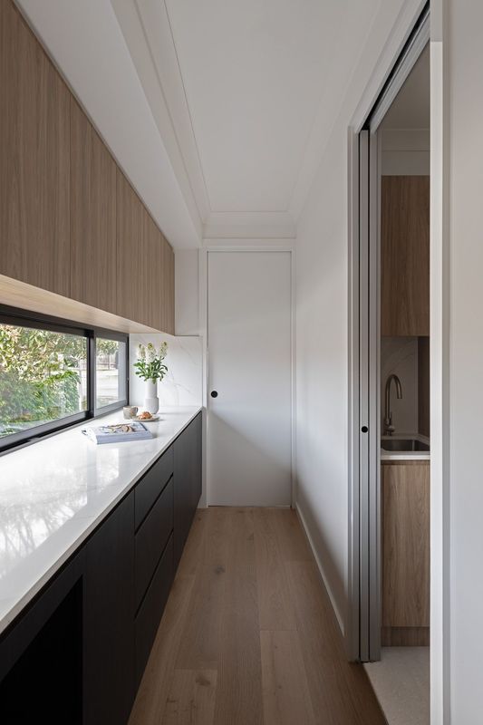 Long, narrow kitchen with wood cabinets, black drawers, a white countertop, and a small sink.