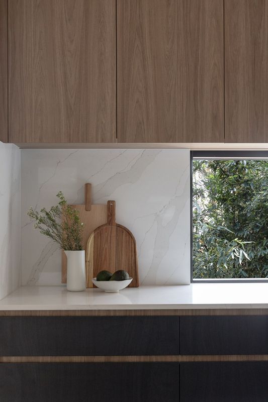Kitchen countertop with cutting boards, vase, and bowl against a marble backsplash, with wood cabinets.