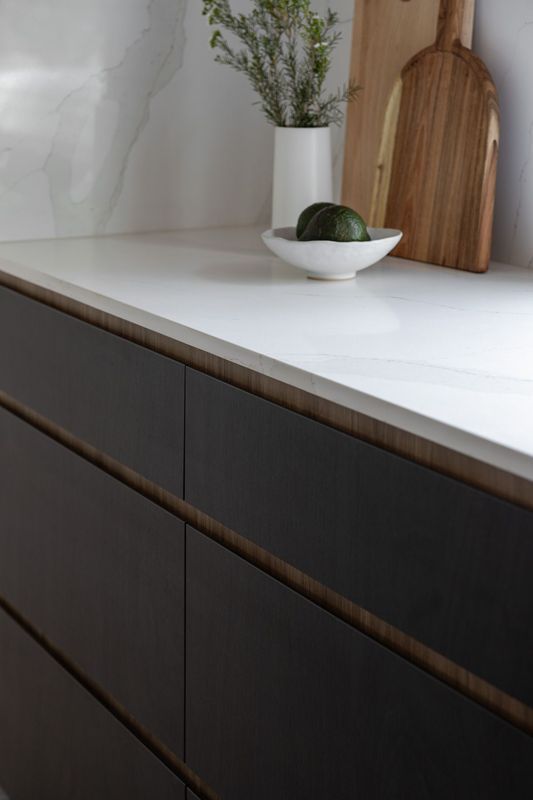 Modern kitchen with dark cabinets, white countertop, wooden accents, and decorative bowl.