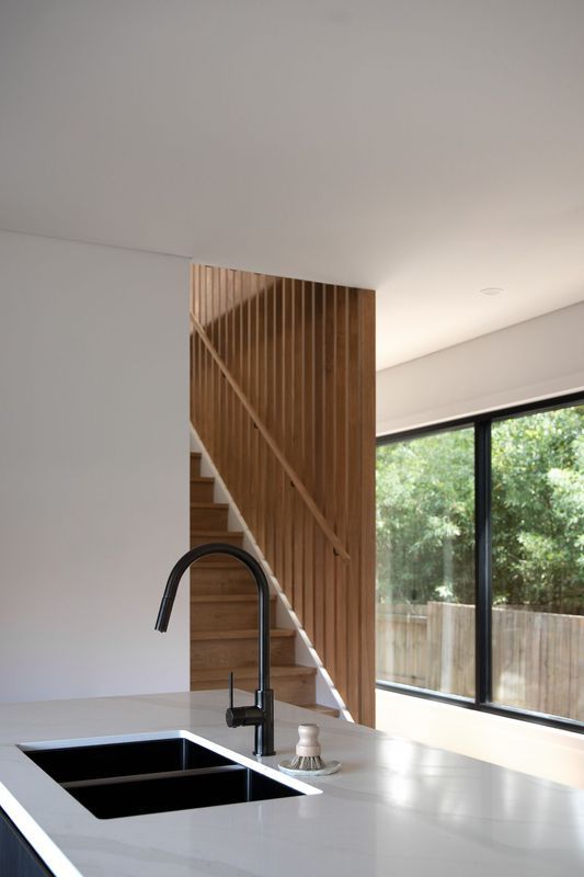 Kitchen with black sink, wooden stairs, and large window with a view of greenery.