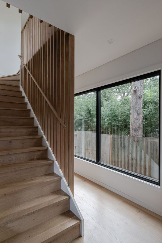 Wooden staircase with wood slat railing next to a large window looking out at trees.