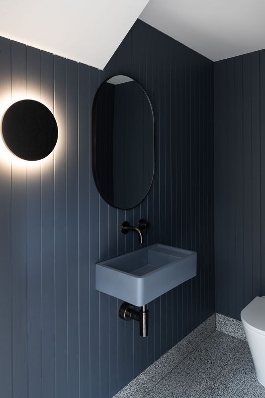 Navy blue bathroom with oval mirror, gray sink, and round wall light.