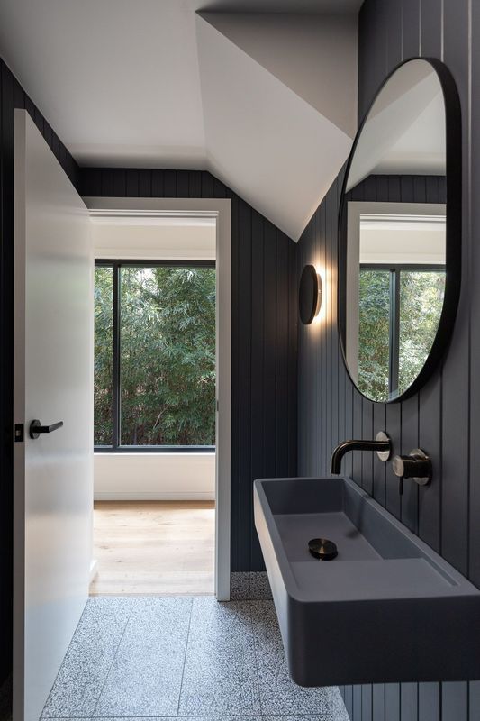 Gray bathroom with a floating sink, oval mirror, and door leading to a room with a window and view of trees.