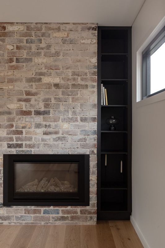 Brick fireplace with black trim, next to tall black bookshelf with some items displayed; wooden floor.