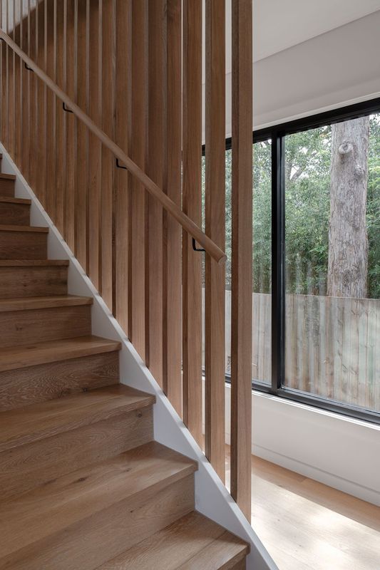 Wooden staircase with vertical wood slats for a railing next to a large window with a tree view.