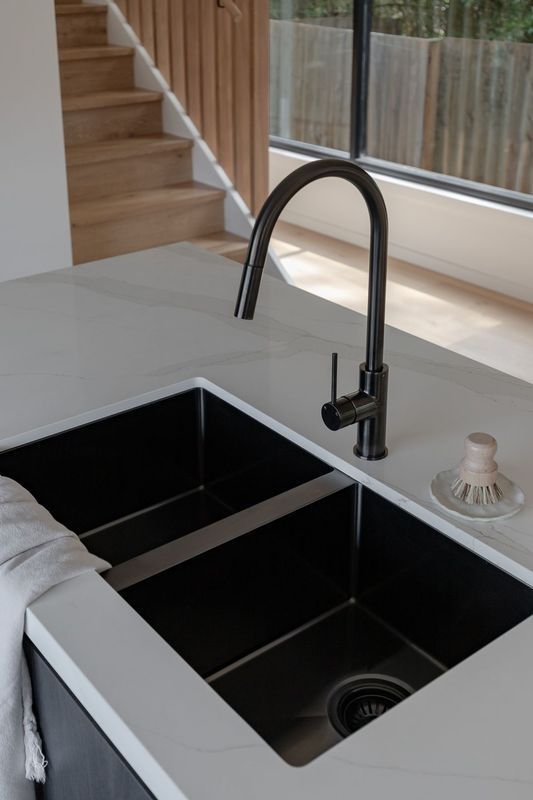 Black double sink in white countertop with a black faucet. Stairs and window in the background.