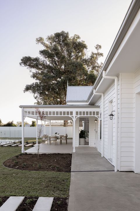 White house exterior with porch, pathway, and lawn; large tree in the background.