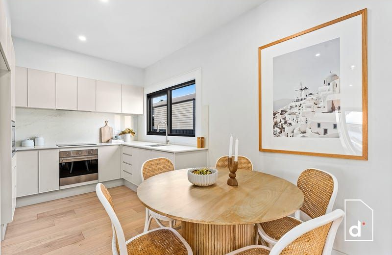 Modern kitchen with light wood floor, round table, and beige cabinets. Framed art on the wall.