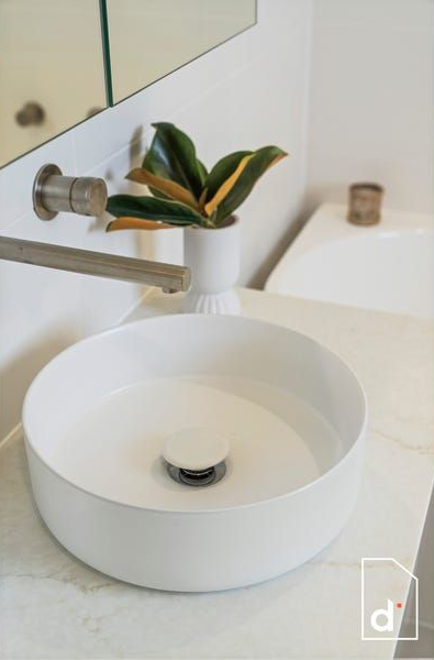 White round vessel sink with a silver faucet and a plant in a white pot.