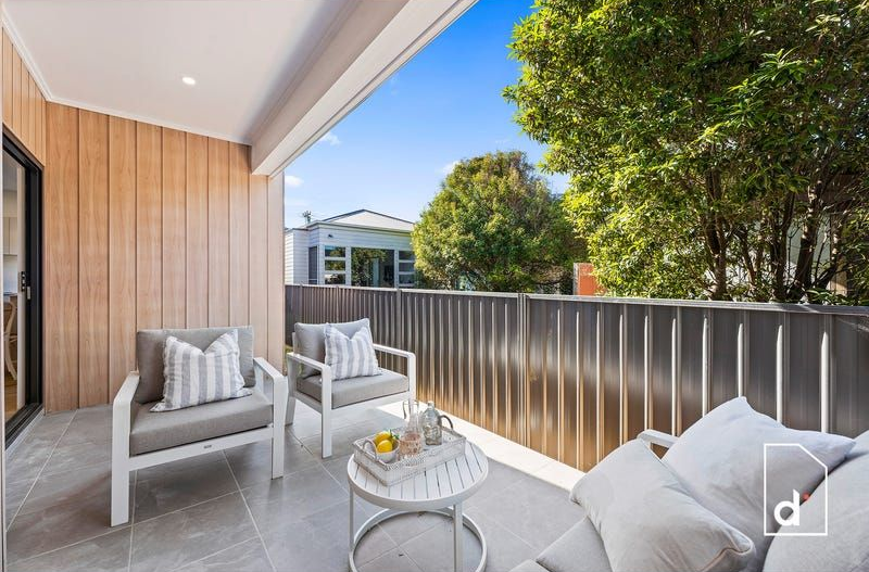 Balcony with seating, wooden wall, gray floor, bright sky, and lush greenery.