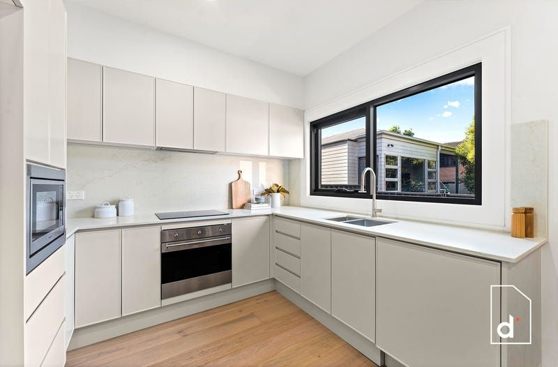 Modern kitchen with white cabinets, stainless steel appliances, and a window with an outdoor view.