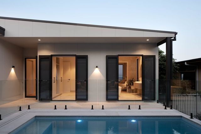 Poolside exterior with open black-framed doors to a room, lit with sconces.