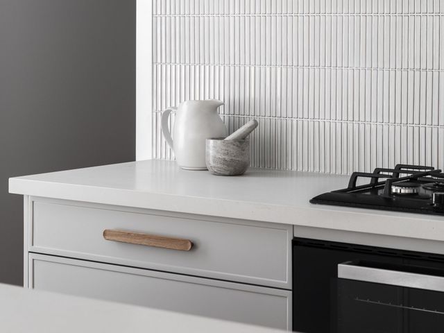 Kitchen countertop with white backsplash, pitcher, mortar, and gas stove.