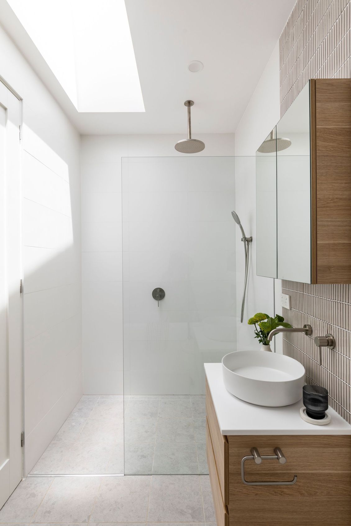 Modern white bathroom with glass shower, wooden vanity, and neutral-toned accent wall.