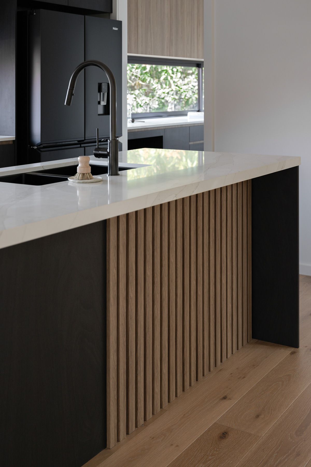 Modern kitchen island with black base, light wood vertical slats, and white countertop.