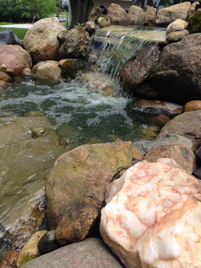 A waterfall is surrounded by rocks and a large rock in the foreground.
