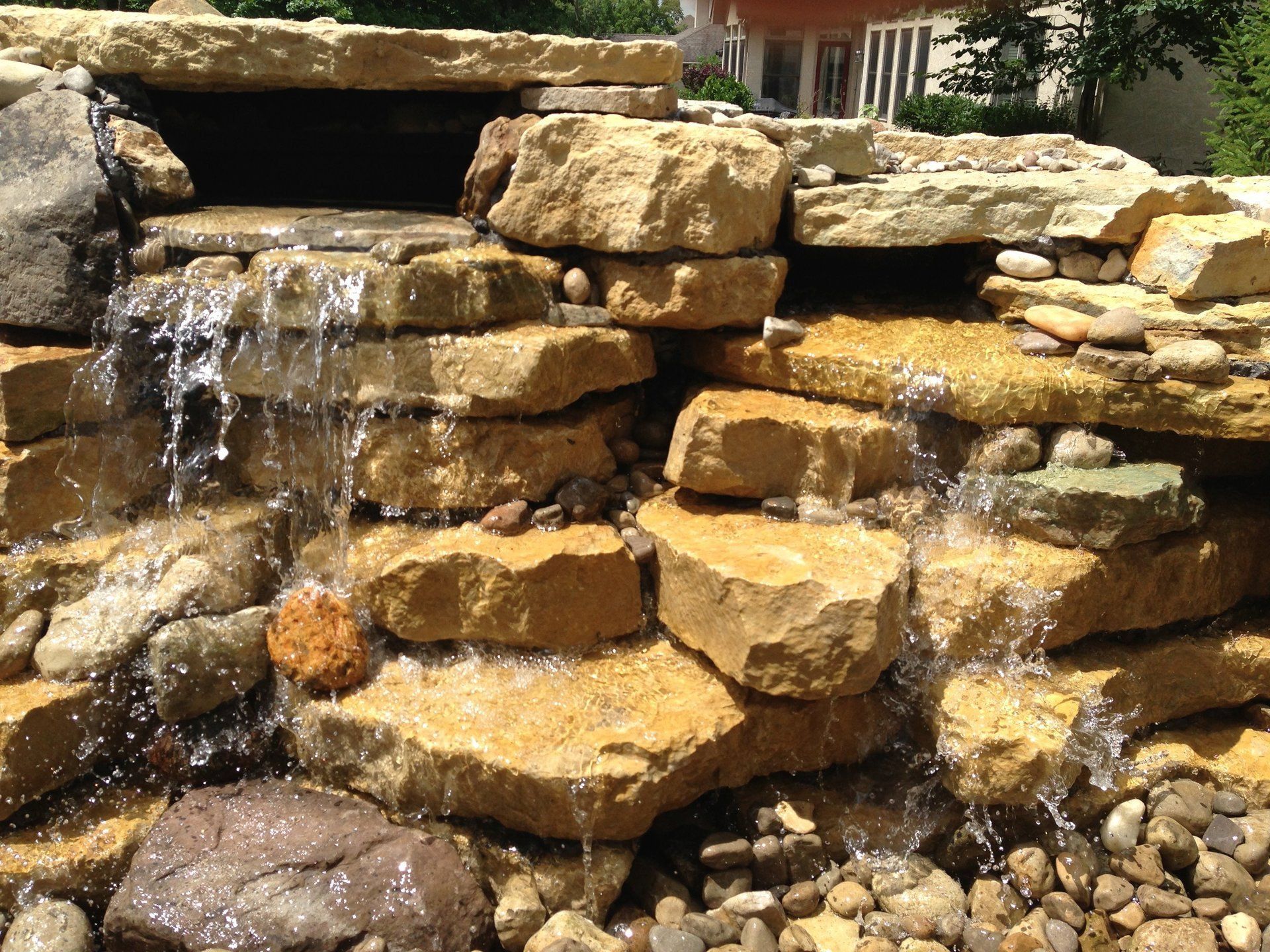 A waterfall is surrounded by rocks and a house in the background