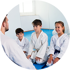 a group of children in karate uniforms are sitting in a circle with their teacher .