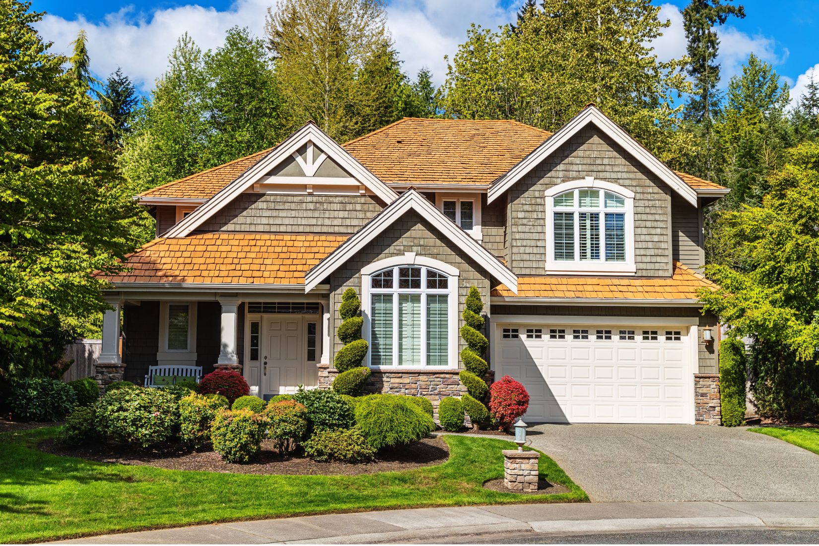 A large house with a white garage door is surrounded by trees.